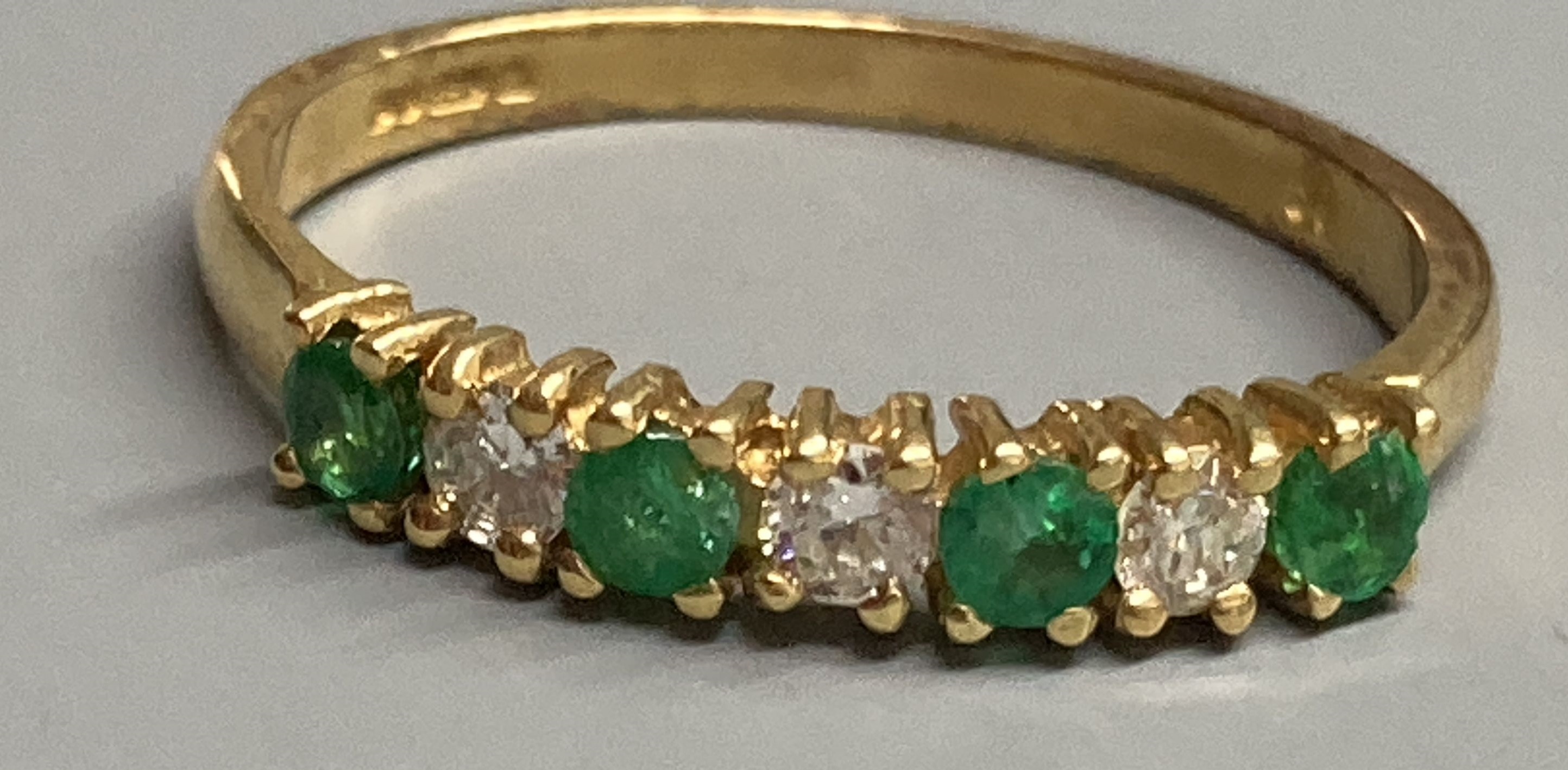 A modern 18ct gold, four stone emerald and three stone diamond set half hoop ring, size M/N, gross 2.1 grams.